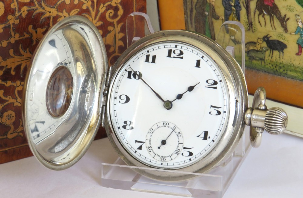An open silver half hunter pocket watch featuring a white enamel dial with black Arabic numerals, a sub-seconds dial, and a polished silver casing.