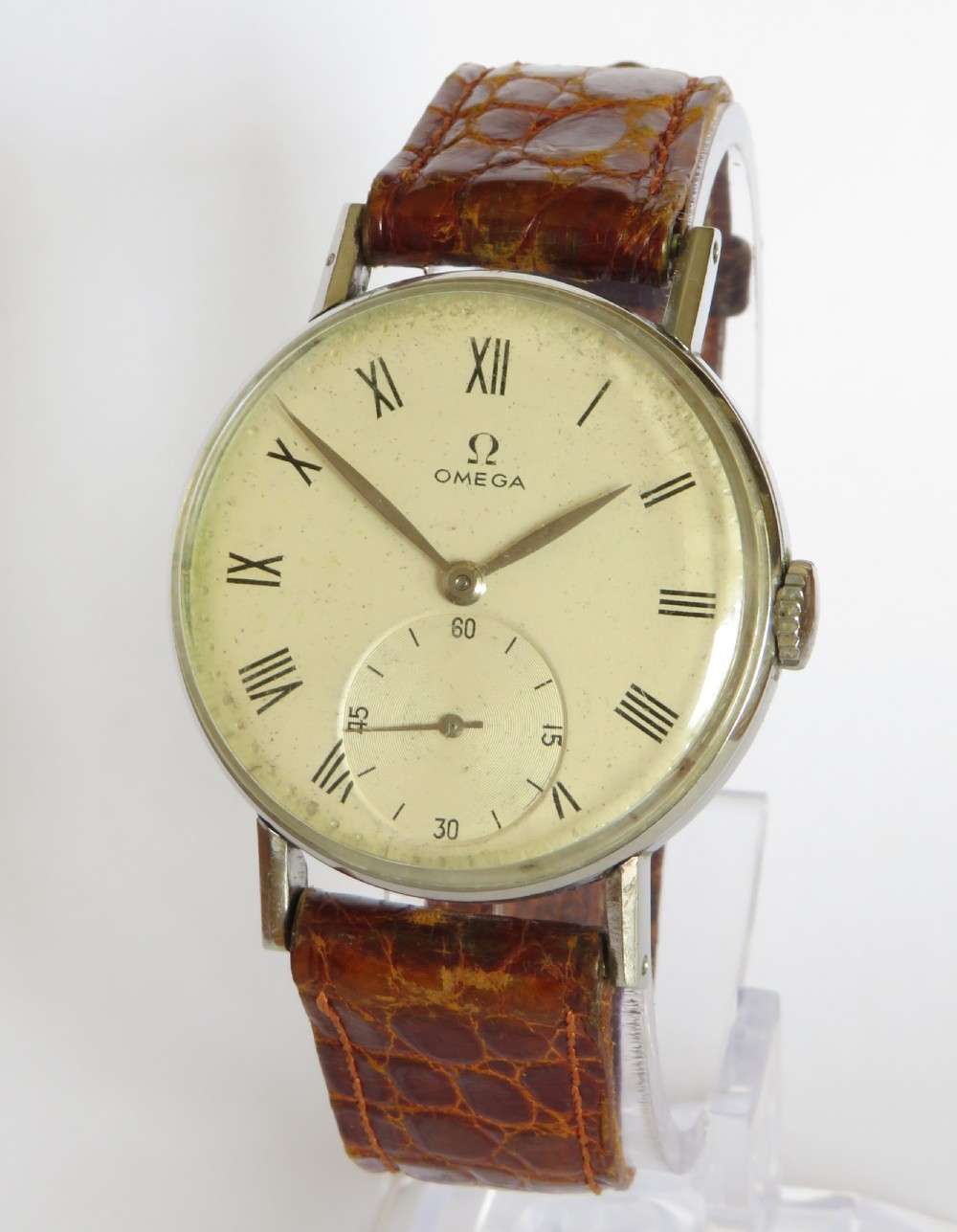 A 1944 vintage gentlemans Omega wristwatch featuring a round silver-tone case, cream dial with black Roman numerals, a sub-seconds dial at six oclock, and a textured brown leather strap.