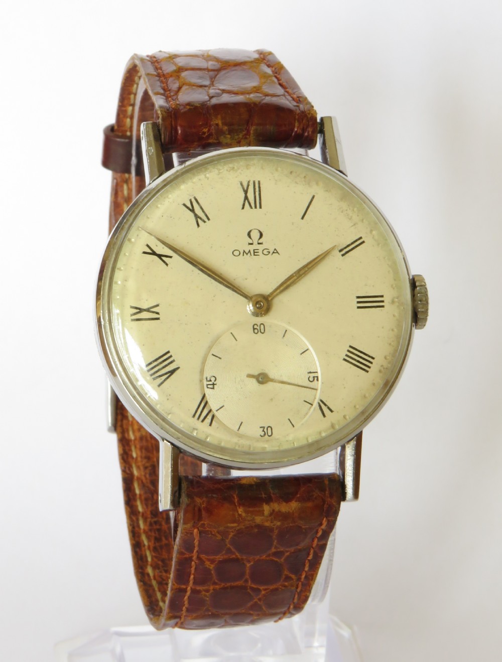 A 1944 vintage gentlemans Omega wristwatch featuring a round silver-tone case, cream dial with black Roman numerals, a sub-seconds dial at six oclock, and a textured brown leather strap. View II