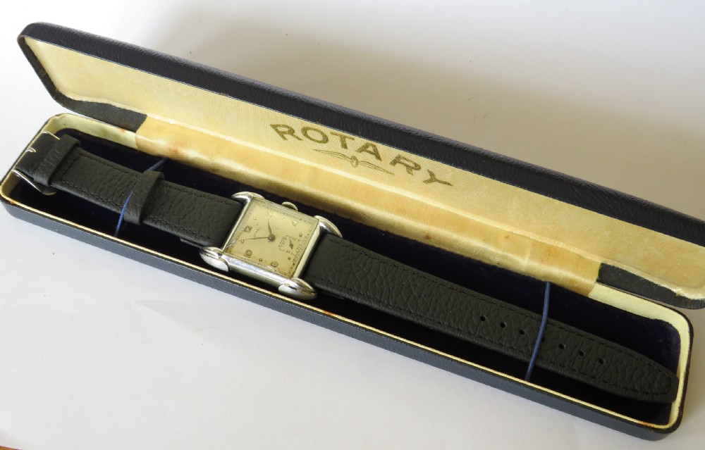 A 1950s gents Rotary wristwatch featuring a rectangular silver-tone case, cream dial with Arabic numerals, sub-seconds dial, and a black leather strap. View V