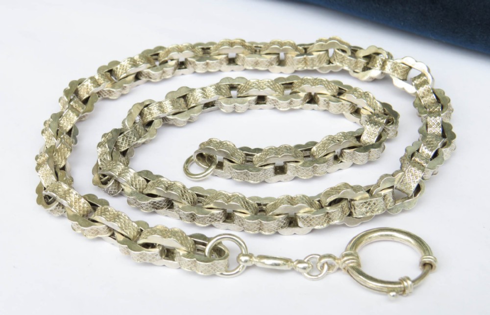An antique silver watch chain featuring textured scalloped links arranged in a loop with a bolt ring fastener.