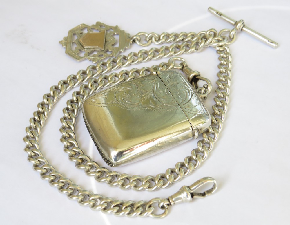 An antique sterling silver curb link Albert watch chain complete with a T-bar, swivel clasp, pierced shield fob, and an engraved rectangular vesta case.