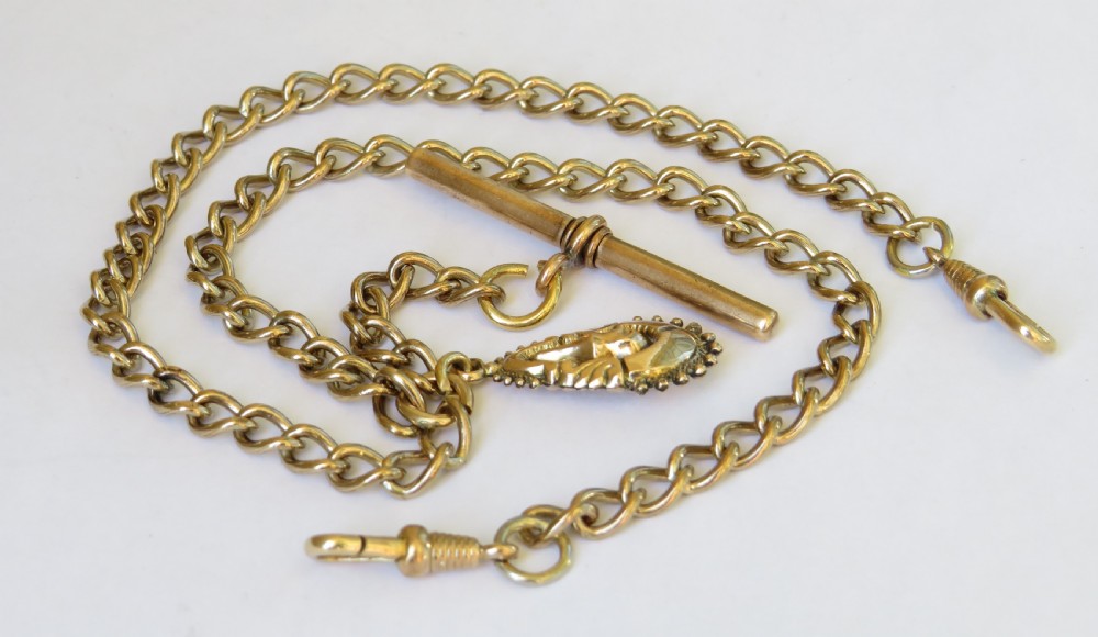 An antique rolled gold double Albert pocket watch chain featuring curb links, a central T-bar, two swivel clasps, and a decorative drop fob pendant.