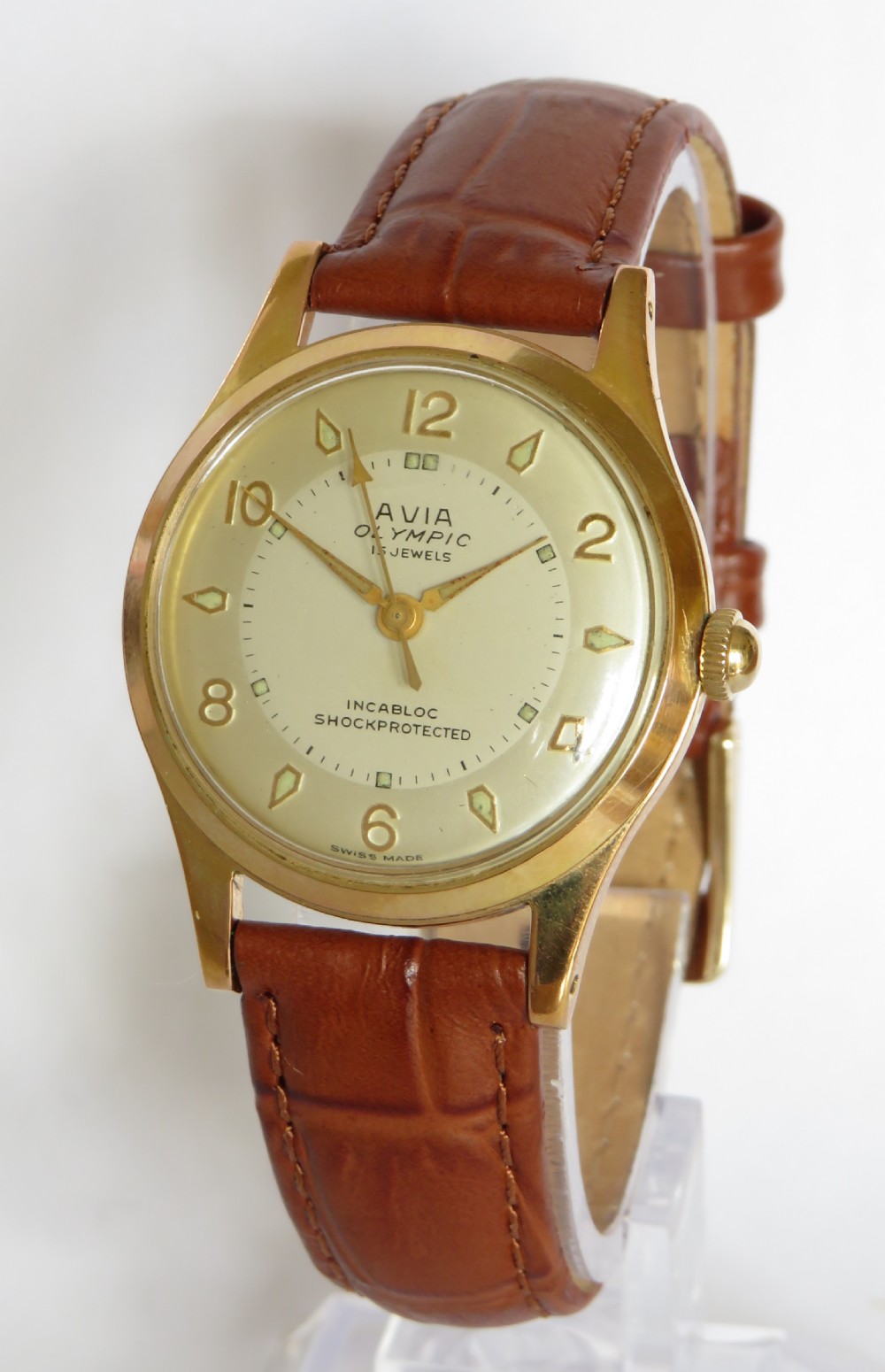 A gents 1960s Avia Olympic wrist watch featuring a gold-toned circular case, cream dial with Arabic numerals, and a brown leather strap.