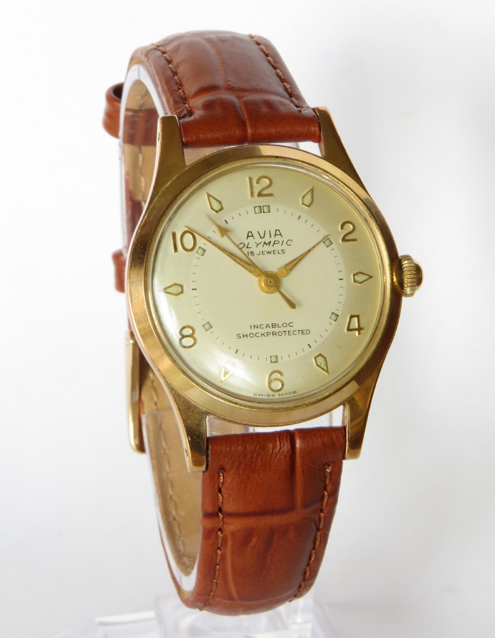 A gents 1960s Avia Olympic wrist watch featuring a gold-toned circular case, cream dial with Arabic numerals, and a brown leather strap. View II