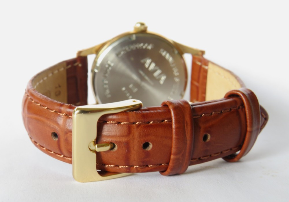 A gents 1960s Avia Olympic wrist watch featuring a gold-toned circular case, cream dial with Arabic numerals, and a brown leather strap. View IV