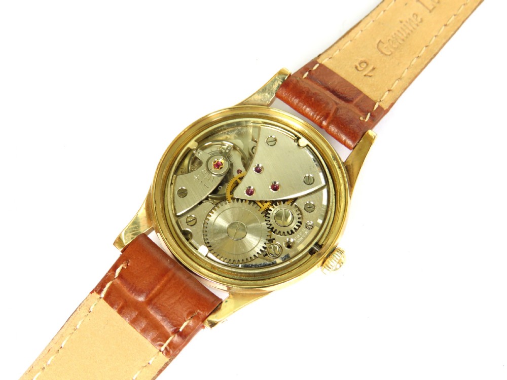 A gents 1960s Avia Olympic wrist watch featuring a gold-toned circular case, cream dial with Arabic numerals, and a brown leather strap. View V