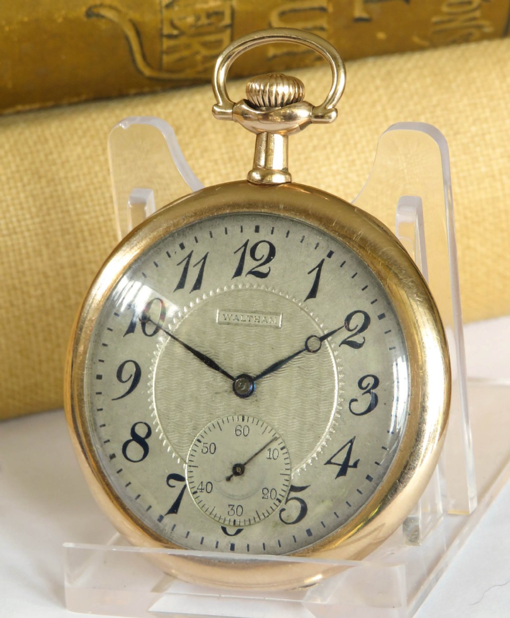 An Edwardian open-face pocket watch featuring a gold-toned casing, dark Arabic numerals, an engine-turned dial centre, and a lower sub-seconds dial.