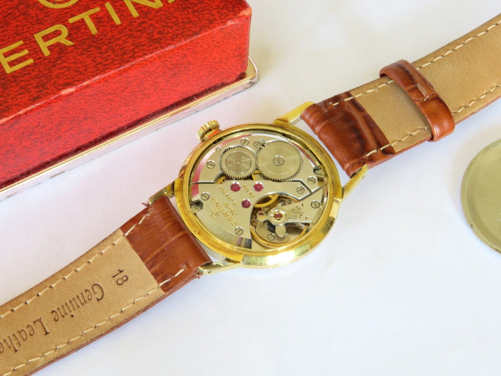 A 1960s Certina gents wristwatch featuring a gold dial, baton hour markers, and a brown leather strap alongside its red presentation box. View III