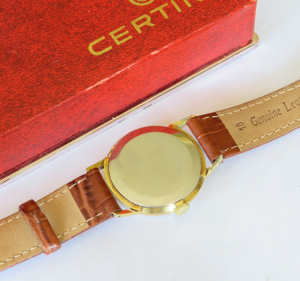 A 1960s Certina gents wristwatch featuring a gold dial, baton hour markers, and a brown leather strap alongside its red presentation box. View V