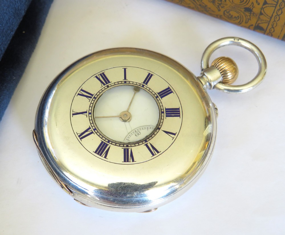 A late Victorian sterling silver half hunter pocket watch featuring dark blue enamel Roman numerals on the outer cover and a central glass window.