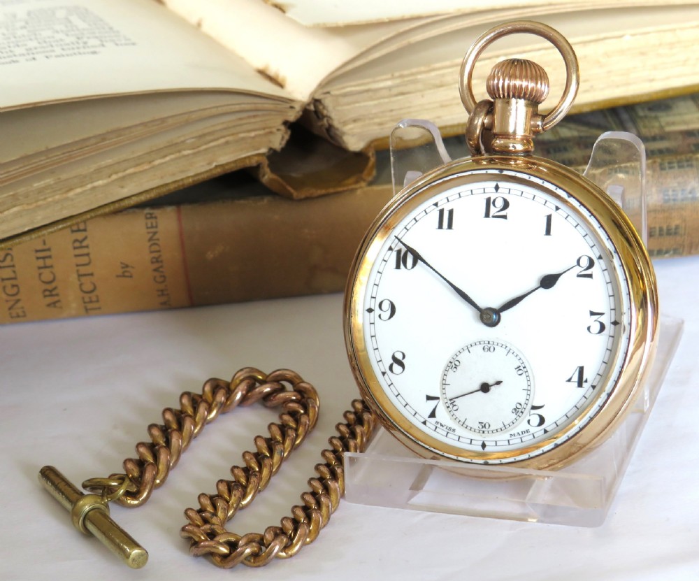 A gold-toned 1930s Cyma stem-winding pocket watch with a white enamel dial, black Arabic numerals, and a curb-link Albert chain with a T-bar.