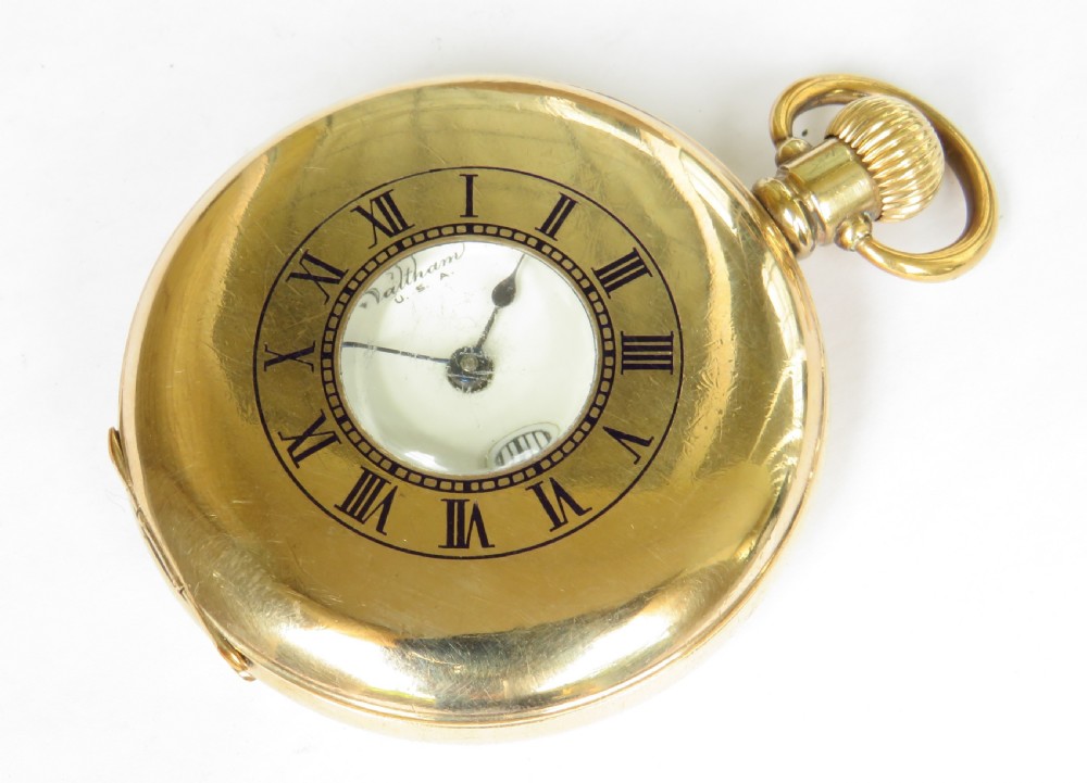 A gold-toned antique Waltham half hunter pocket watch featuring a central glass window surrounded by black Roman numerals on the outer casing.