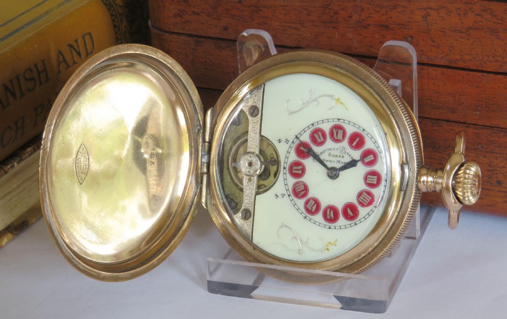 An open full hunter pocket watch featuring a gold case, a cream enamel dial with red Roman numeral cartouches, and an exposed balance bridge.