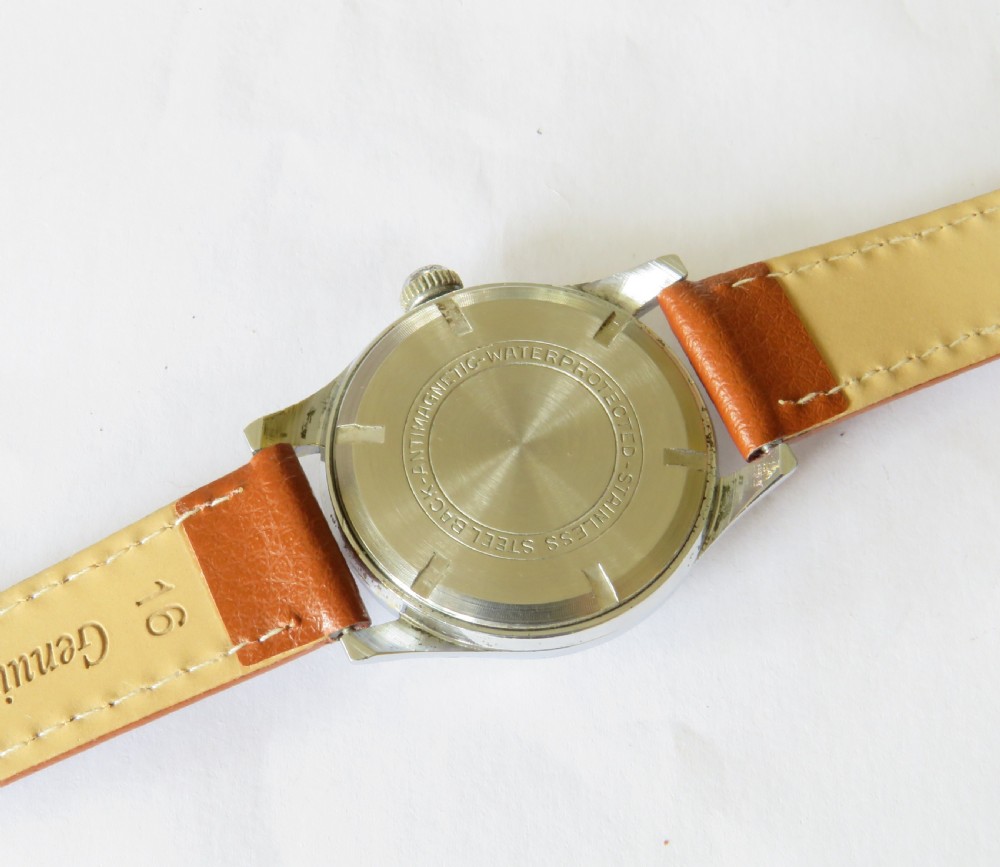 A 1950s gents mechanical wristwatch featuring a round metal case, cream two-tone dial with Arabic numerals, sub-seconds dial, and a tan leather strap. View IV