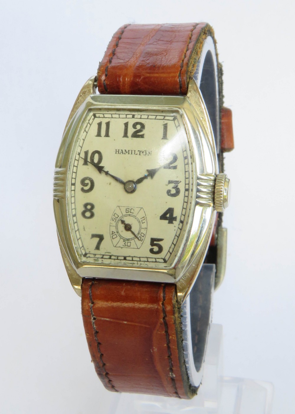 A 1930s Art Deco gents Hamilton wristwatch with a gold-toned tonneau case, cream dial, Arabic numerals, sub-seconds dial, and brown leather strap.