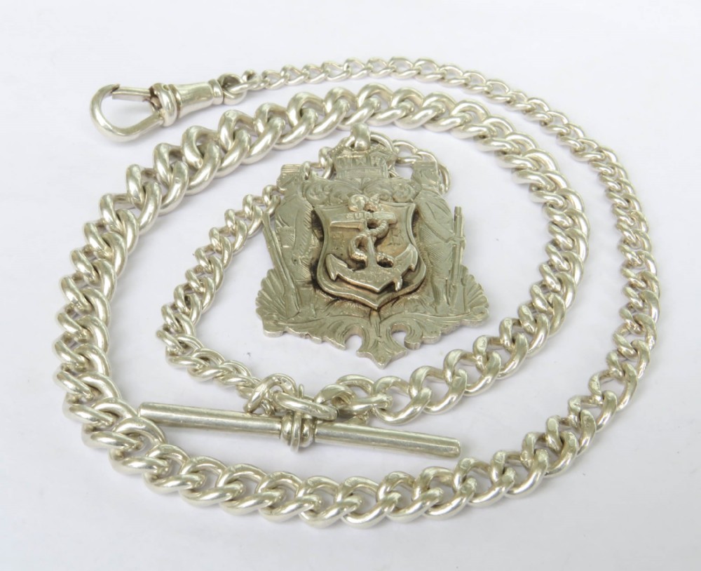 An antique silver Albert watch chain featuring thick curb links, a T-bar fastener, a swivel dog clip clasp, and an ornate heraldic coat of arms fob depicting an anchor motif.