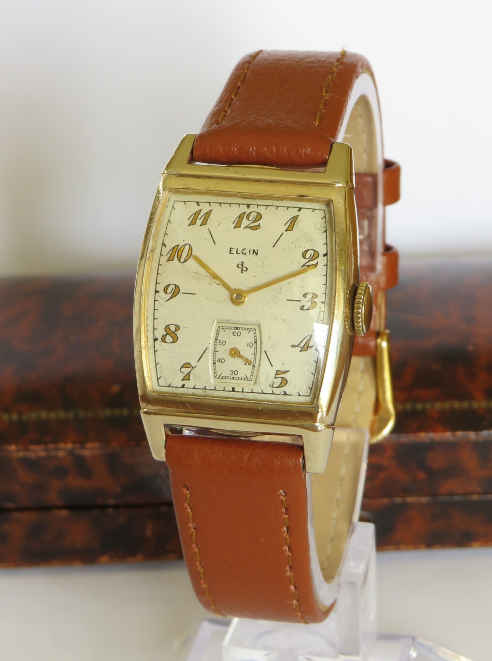 A 1948 Elgin mens wristwatch featuring a rectangular gold-toned case, cream dial with gold Arabic numerals, sub-seconds dial, and tan leather strap.