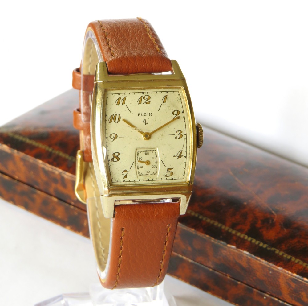 A 1948 Elgin mens wristwatch featuring a rectangular gold-toned case, cream dial with gold Arabic numerals, sub-seconds dial, and tan leather strap. View II