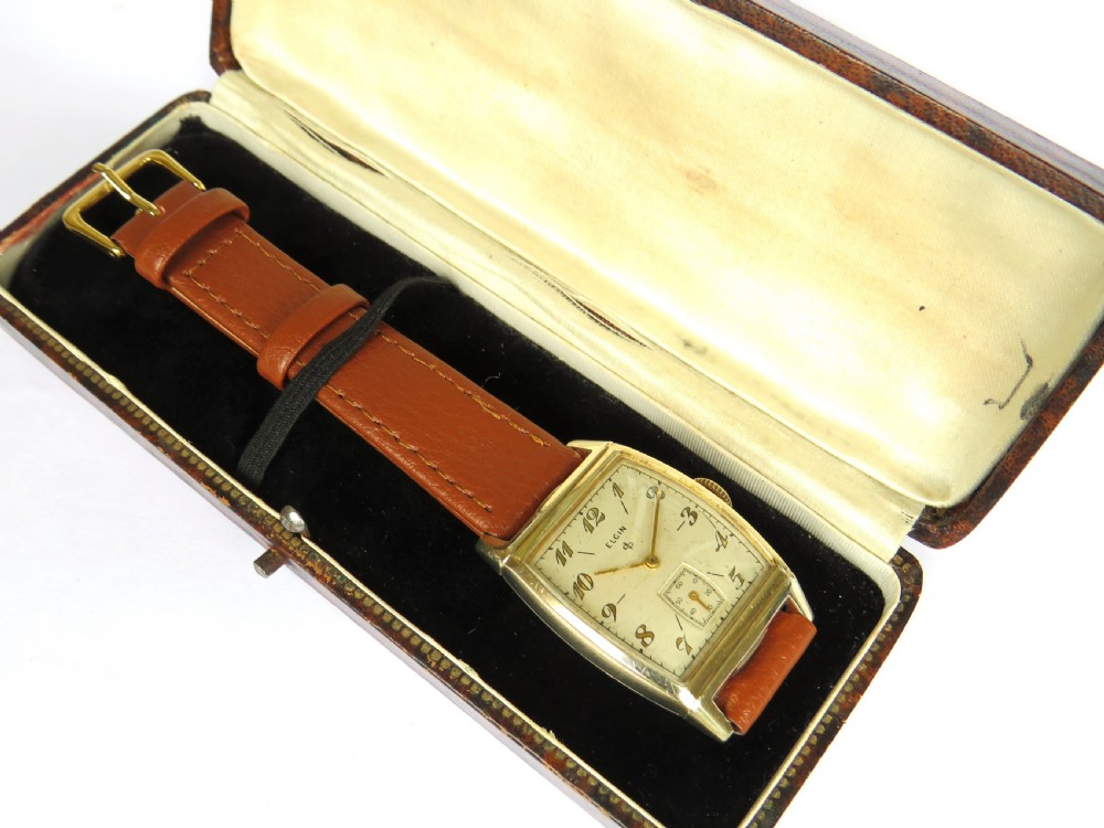 A 1948 Elgin mens wristwatch featuring a rectangular gold-toned case, cream dial with gold Arabic numerals, sub-seconds dial, and tan leather strap. View III