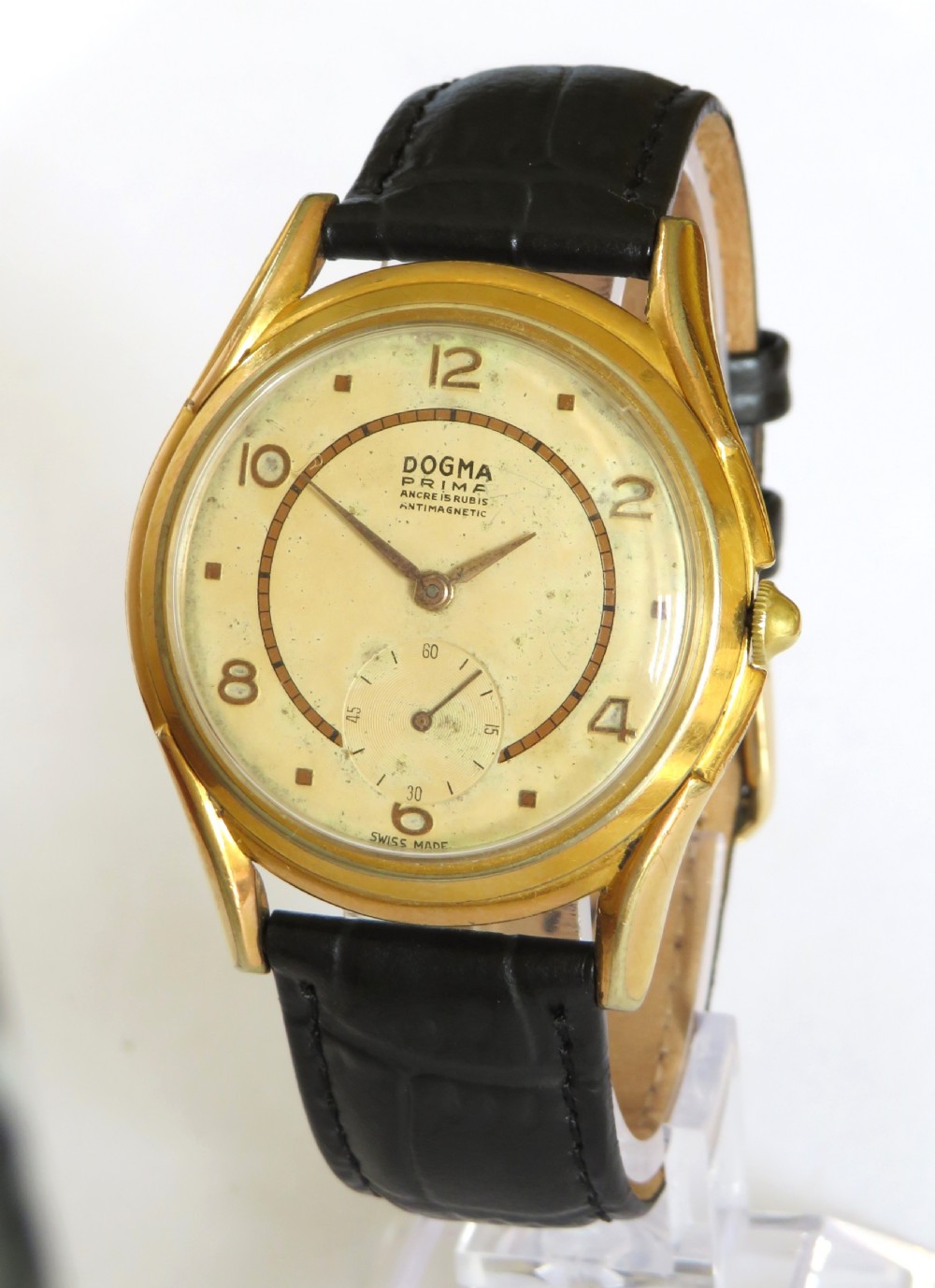 A 1950s gents Dogma Prima wristwatch featuring a gold-toned case, champagne dial with sub-seconds subdial, and black leather strap.