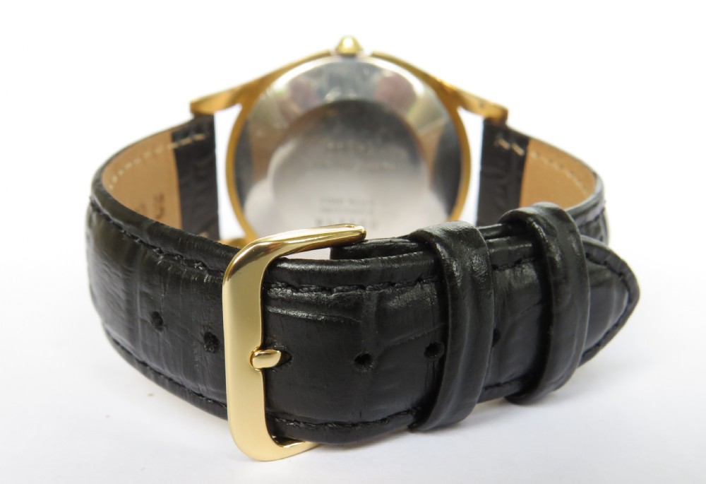 A 1950s gents Dogma Prima wristwatch featuring a gold-toned case, champagne dial with sub-seconds subdial, and black leather strap. View V