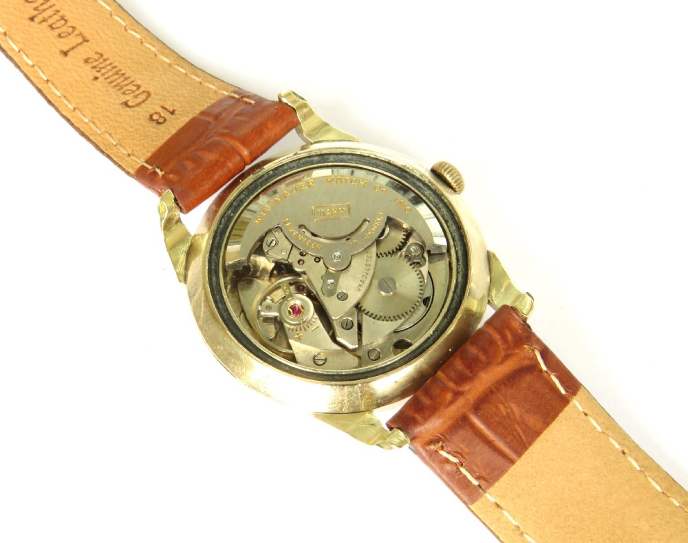 A mens 1950s Wittnauer automatic wristwatch featuring a circular gold-plated case, cream dial with dart hour markers, and a brown leather crocodile-embossed strap. View III