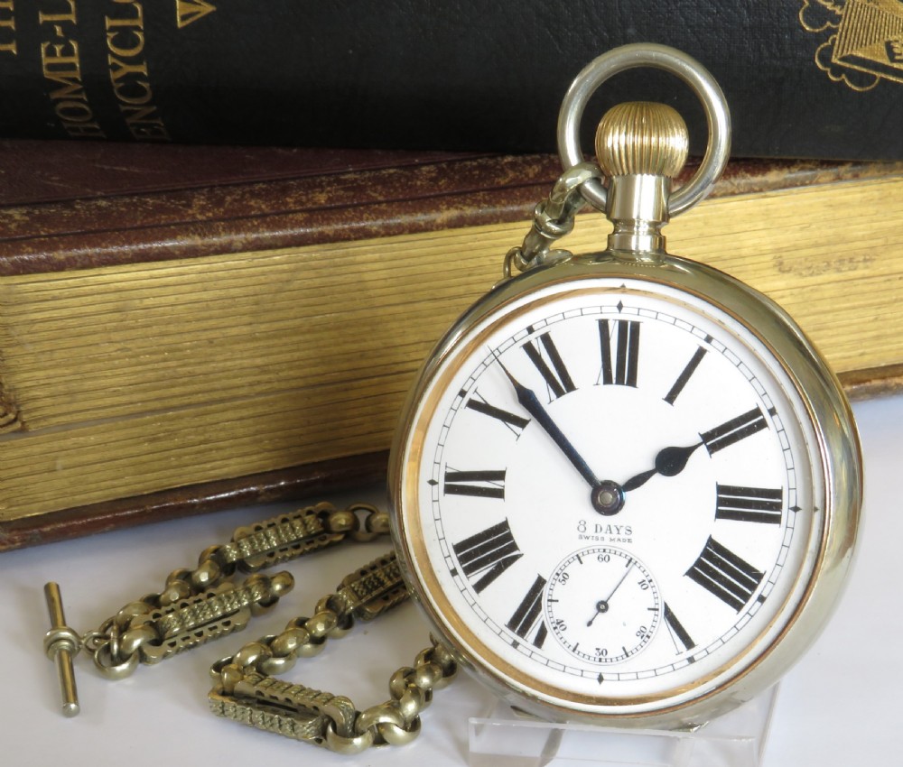 An antique nickel-cased goliath open-face pocket watch featuring a white enamel dial with Roman numerals, an eight-day movement marking, and an attached decorative brass chain.