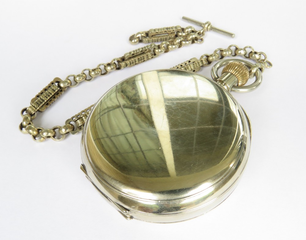 An antique nickel-cased goliath open-face pocket watch featuring a white enamel dial with Roman numerals, an eight-day movement marking, and an attached decorative brass chain. View V