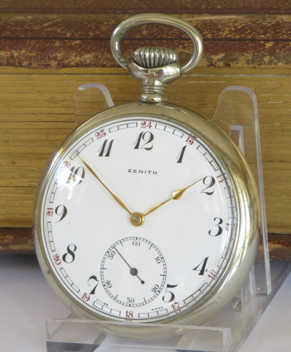 A 1939 Zenith open-face pocket watch featuring a white enamel dial with black Arabic numerals, secondary red 24-hour markers, a subsidiary seconds dial, and a metallic silver case. View II