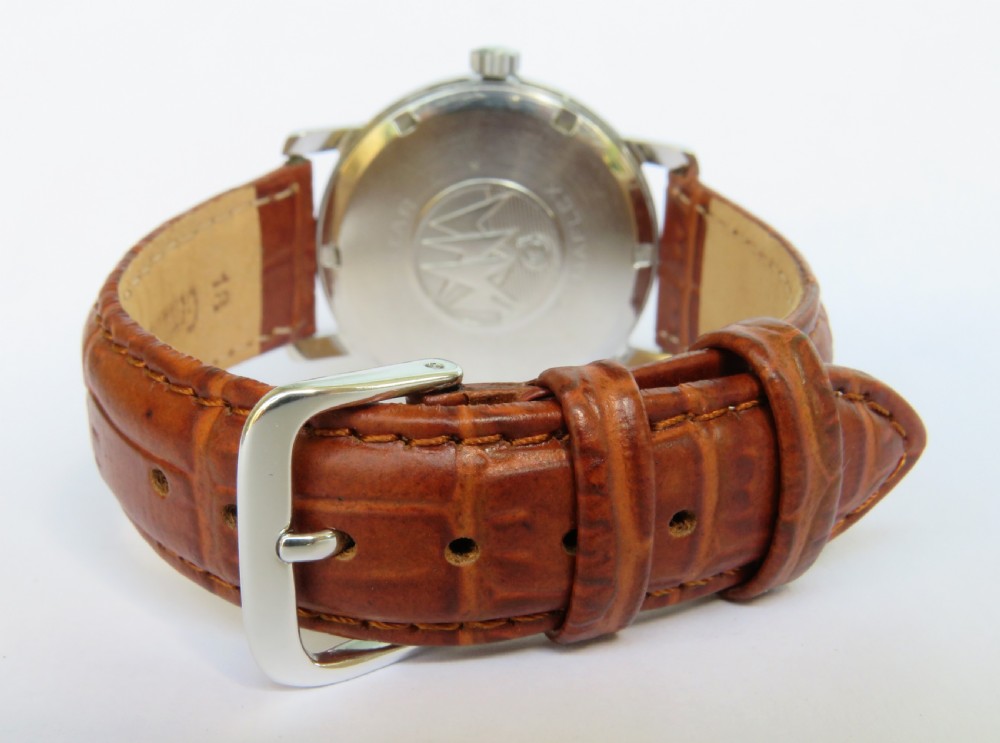 A 1950s Cyma Watersport gentlemans wristwatch featuring a light champagne dial with Arabic numerals, a metallic case, and a textured brown leather strap. View V