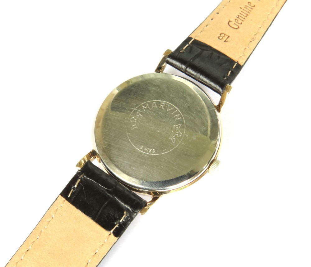 A 1960s vintage Marvin Hermetic gents wrist watch featuring a gold-toned circular case, champagne dial with applied baton hour markers, and a textured black leather strap. View IV