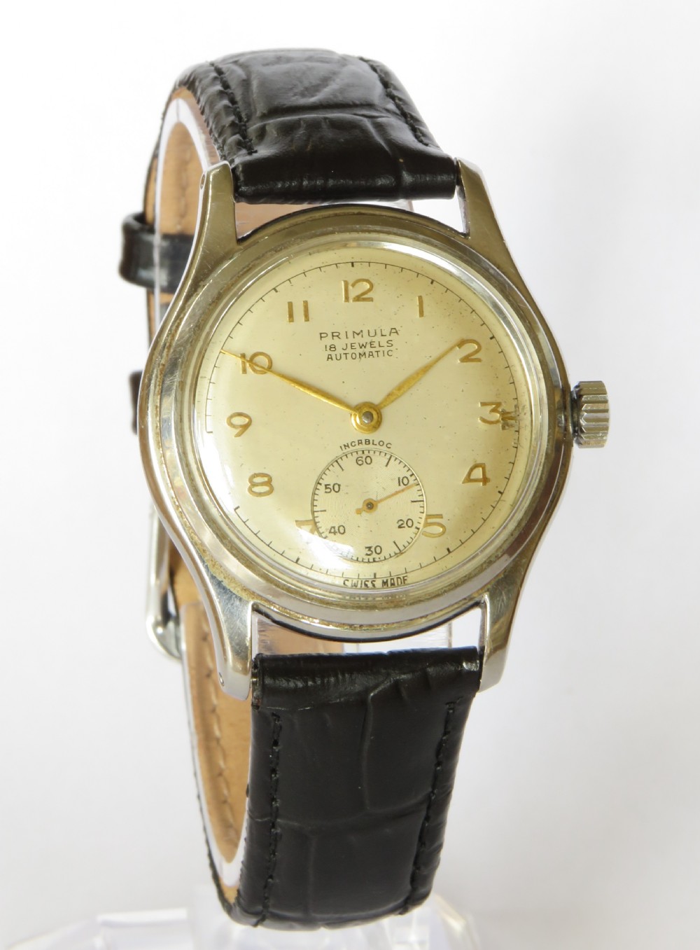 A 1950s gentlemens Primula Swiss automatic wristwatch featuring a silver-tone case, cream dial with gold-tone Arabic numerals, sub-seconds dial, and a black leather strap. View II