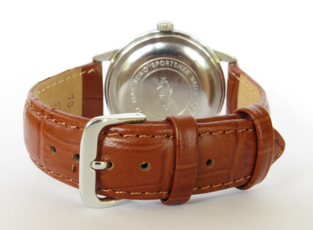 A 1960s gents Seiko Sportsman Diashock wristwatch featuring a silver case, champagne dial with baton indices, and a brown leather strap. View V