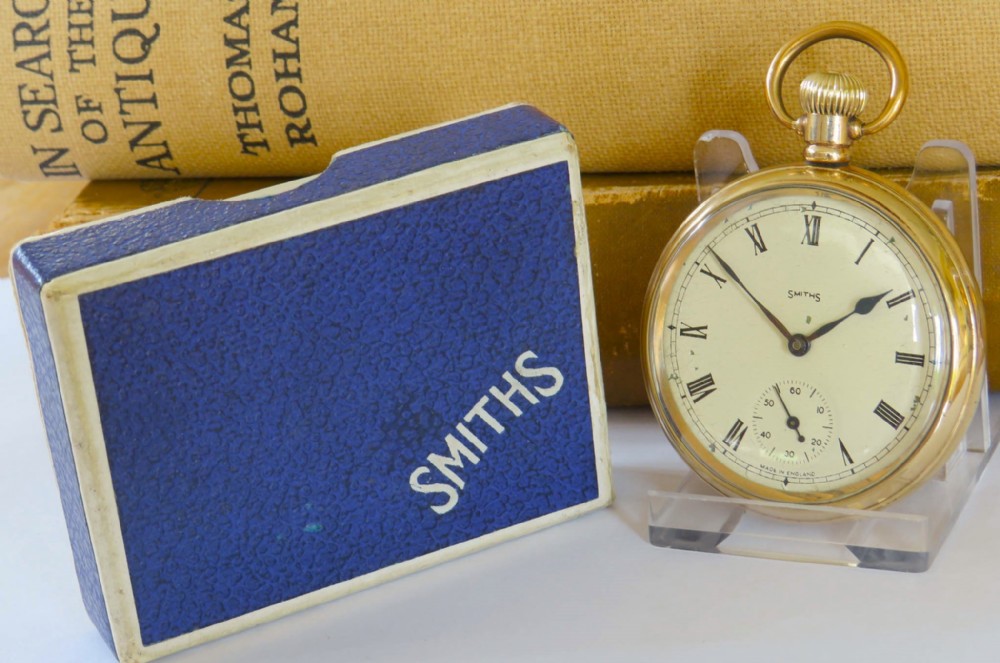 A 1940s Smiths open-face pocket watch with a gold-tone metal case, white Roman numeral dial, and an accompanying textured blue presentation box.