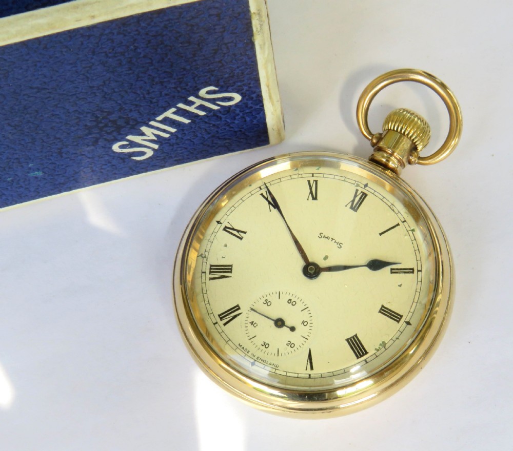A 1940s Smiths open-face pocket watch with a gold-tone metal case, white Roman numeral dial, and an accompanying textured blue presentation box. View II