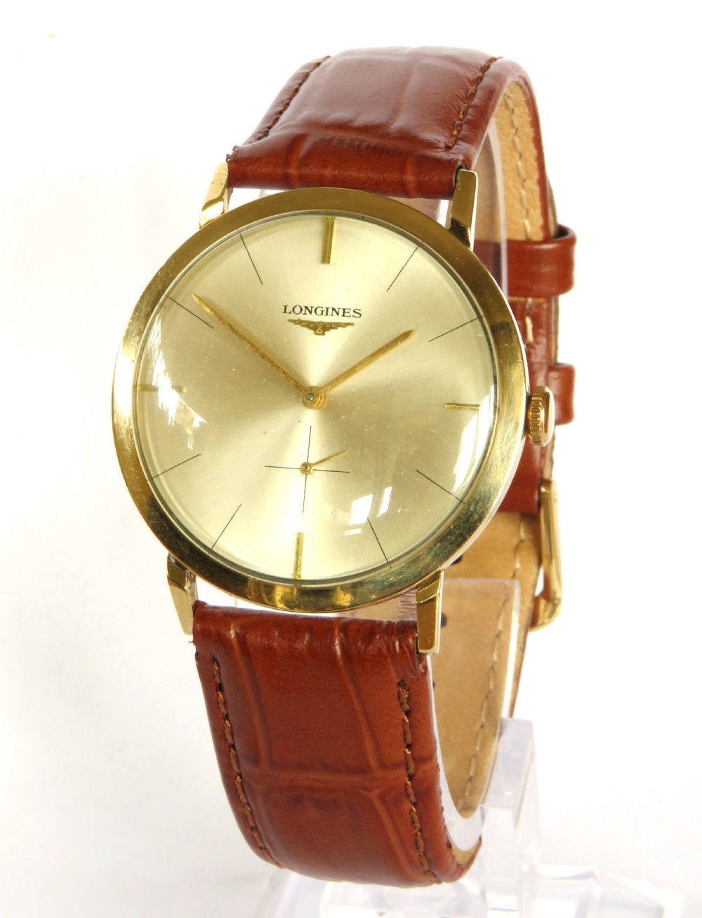 A 1964 gents Longines wristwatch featuring a round 9ct gold case, gold-tone sunburst dial with slim baton markers, sub-second dial at six oclock, and a brown leather strap.