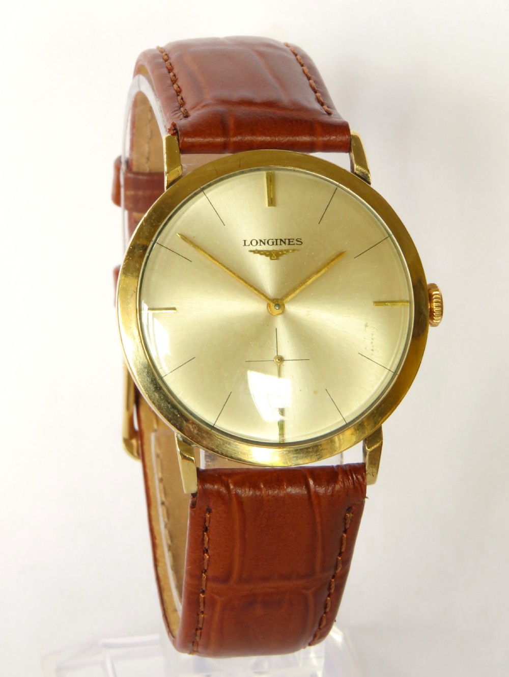 A 1964 gents Longines wristwatch featuring a round 9ct gold case, gold-tone sunburst dial with slim baton markers, sub-second dial at six oclock, and a brown leather strap. View II