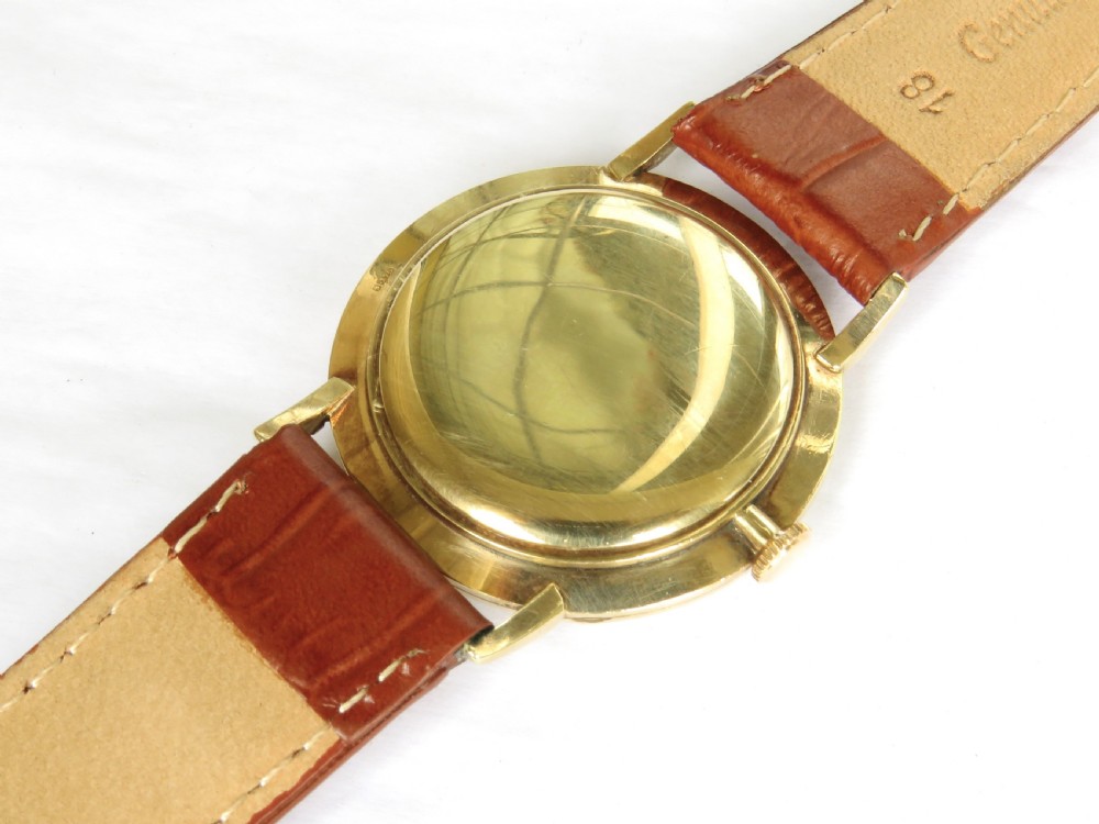 A 1964 gents Longines wristwatch featuring a round 9ct gold case, gold-tone sunburst dial with slim baton markers, sub-second dial at six oclock, and a brown leather strap. View IV