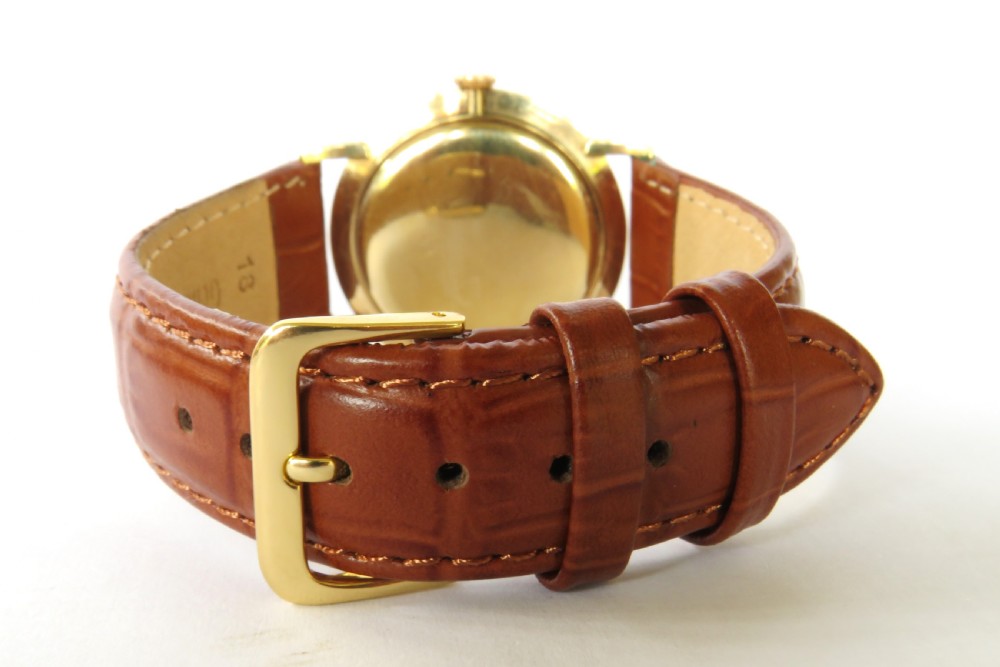 A 1964 gents Longines wristwatch featuring a round 9ct gold case, gold-tone sunburst dial with slim baton markers, sub-second dial at six oclock, and a brown leather strap. View V