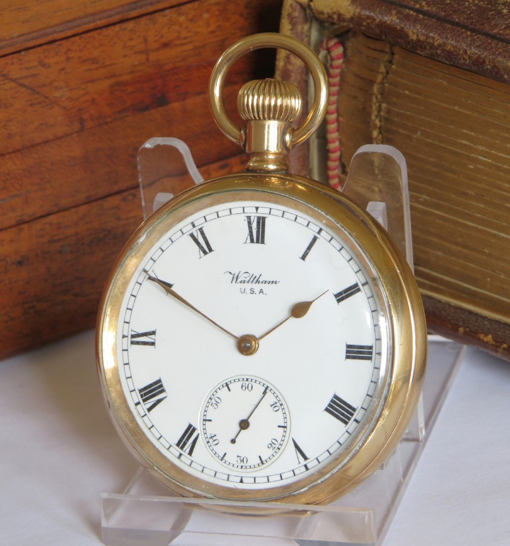 An open-face gold Waltham Traveler pocket watch featuring a white enamel dial with black Roman numerals and a subsidiary seconds dial.