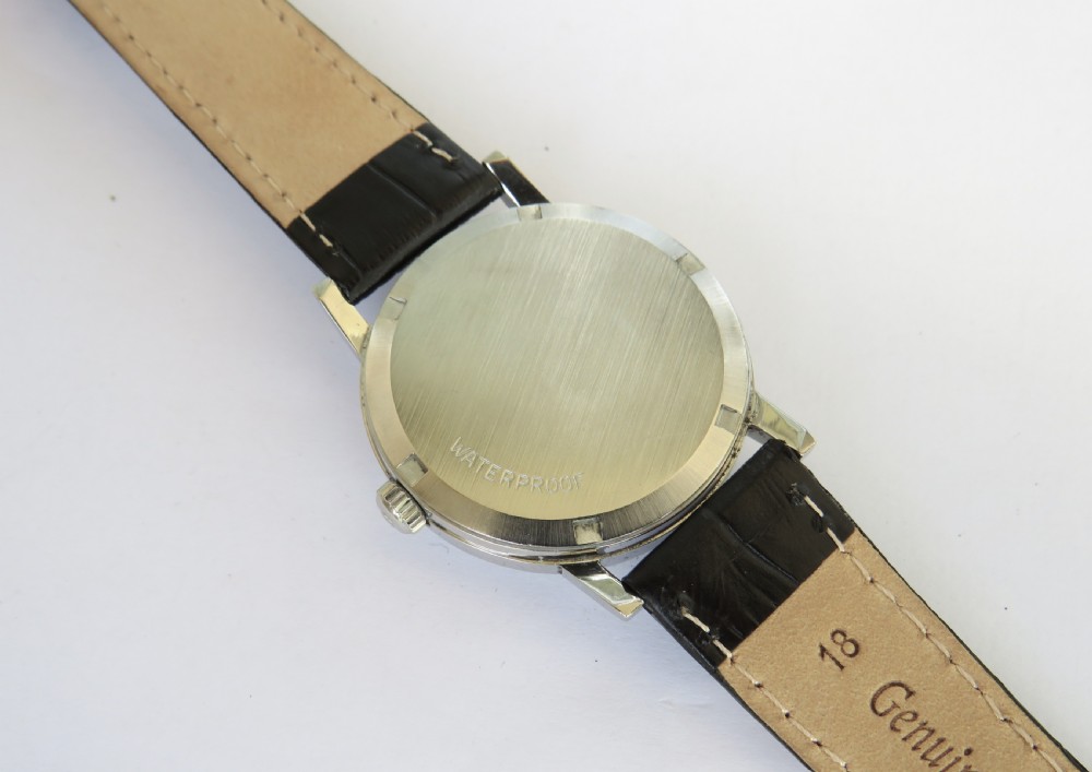 A 1970s gents Omega Geneve wristwatch featuring a round silver-toned dial, black baton hour markers, and a black leather strap. View IV
