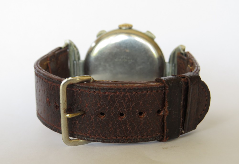 A 1930s gents chronograph wristwatch featuring a patinated cream dial, dual sub-dials, silver-tone case, and a textured brown leather strap. View V