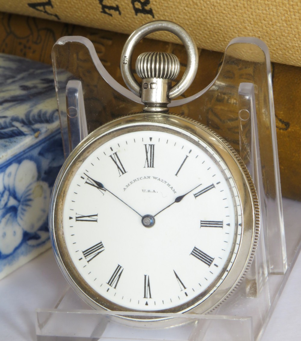 An open-face antique silver pocket watch featuring a white enamel dial with black Roman numerals and steel hands.