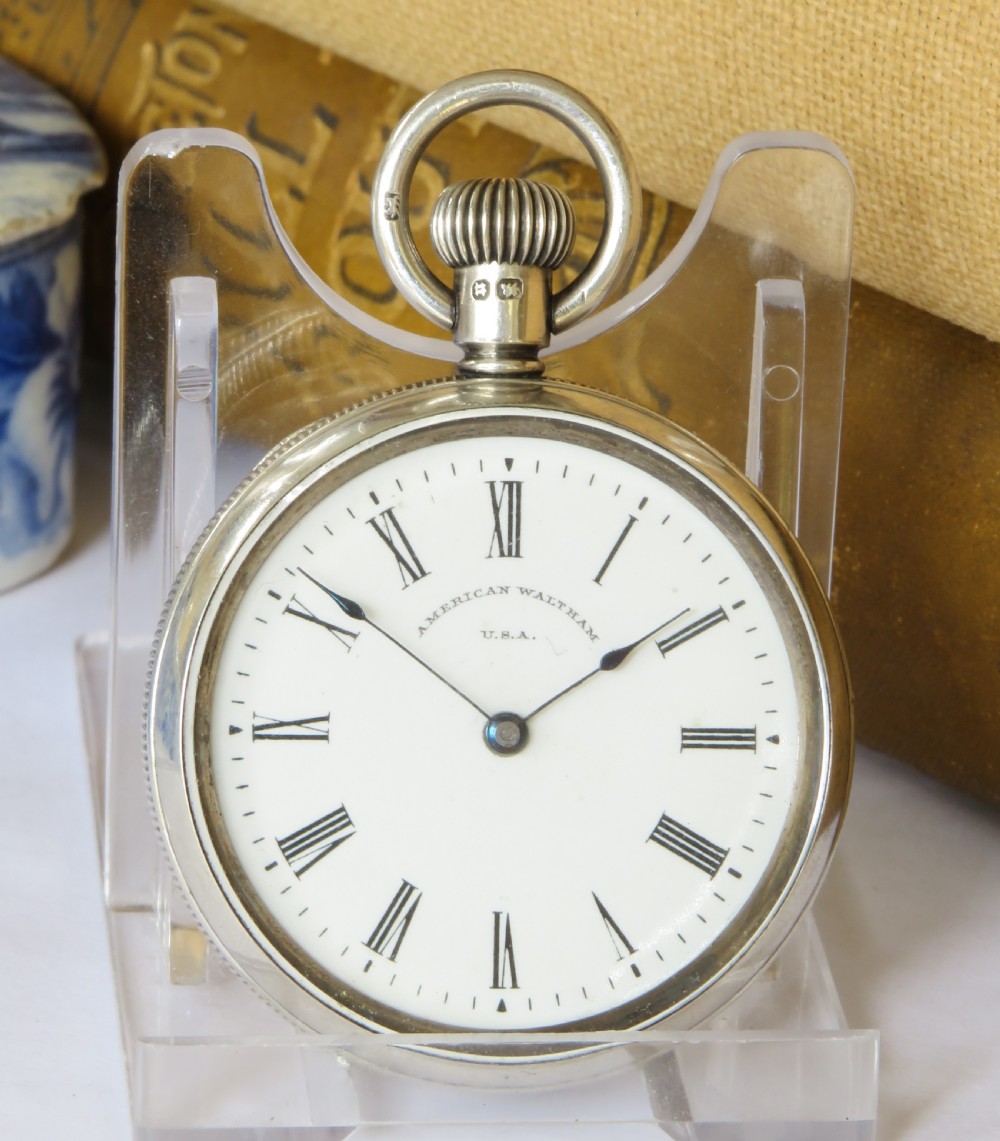 An open-face antique silver pocket watch featuring a white enamel dial with black Roman numerals and steel hands. View II