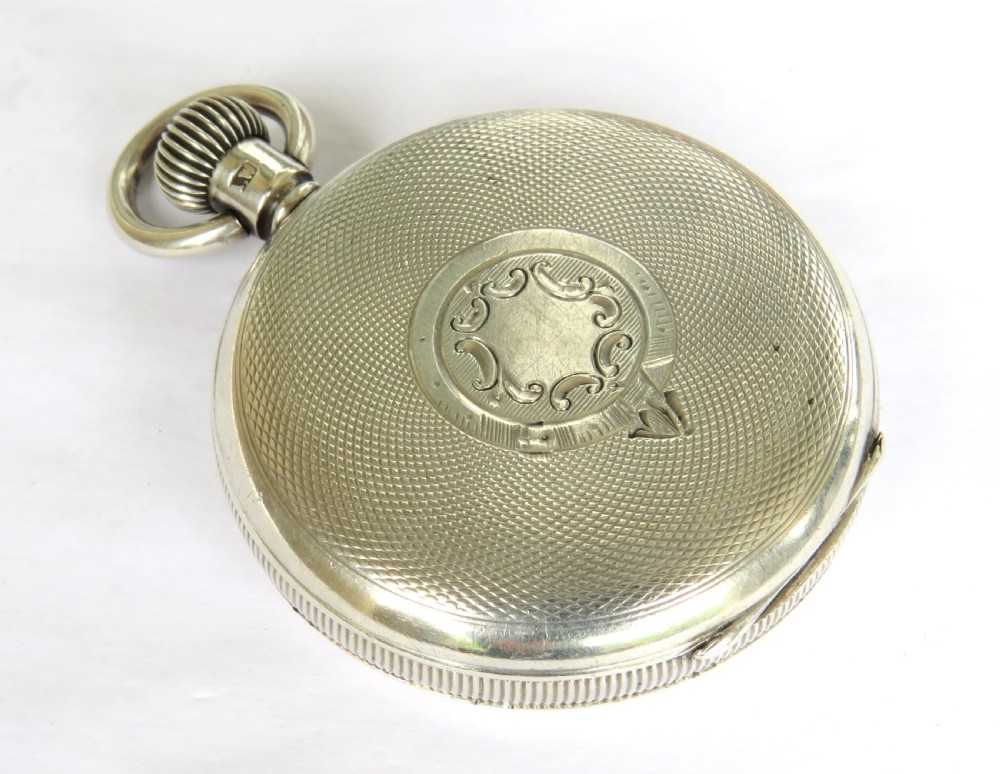 An open-face antique silver pocket watch featuring a white enamel dial with black Roman numerals and steel hands. View V