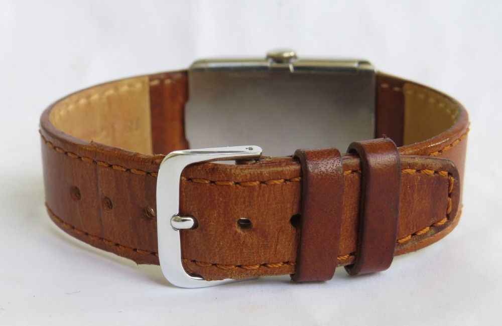 A 1930s rectangular Omega gents wristwatch featuring a silver-tone case, aged cream dial with Arabic numerals, sub-seconds dial, and a tan leather strap. View V