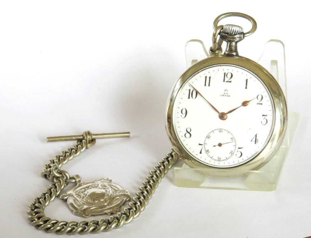 An open-face antique Omega pocket watch with a white enamel dial, black Arabic numerals, a sub-seconds dial, and an attached silver curb link chain with a T-bar and decorative shield fob. View II