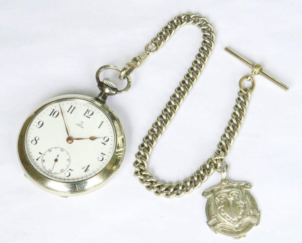 An open-face antique Omega pocket watch with a white enamel dial, black Arabic numerals, a sub-seconds dial, and an attached silver curb link chain with a T-bar and decorative shield fob. View III