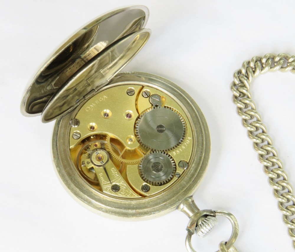 An open-face antique Omega pocket watch with a white enamel dial, black Arabic numerals, a sub-seconds dial, and an attached silver curb link chain with a T-bar and decorative shield fob. View V